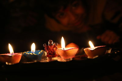 Portrait of boy with ganesha figurine amidst lit diyas at night