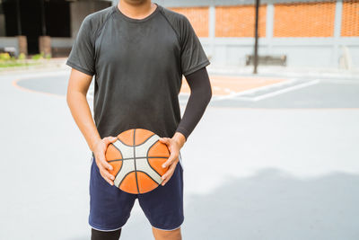 Low section of man holding ball while standing on soccer field