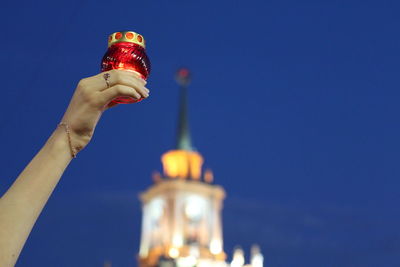 Low angle view of woman hand holding light by illuminated building against clear sky