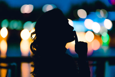 Defocused image of man photographing illuminated lights in city at night