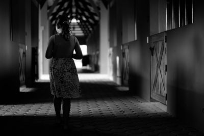 Rear view of girl walking on aisle in stable