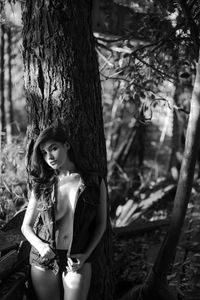 Portrait of seductive woman wearing jacket standing by tree trunk in forest