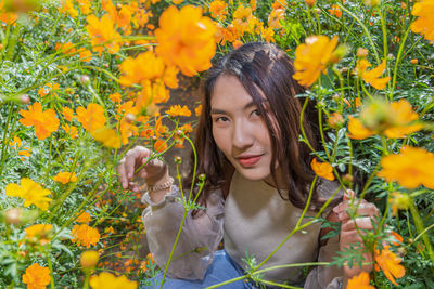 Portrait of woman crouching on land by yellow flowering plants