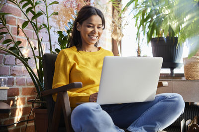 Happy woman using laptop sitting on chair at home