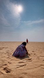 Rear view of woman sitting on sand at beach against sky