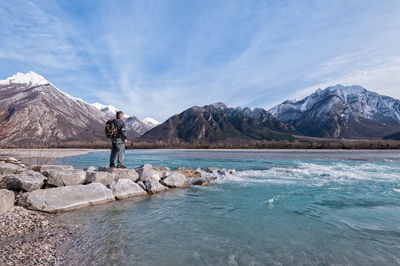 Man standing on rock by lake against sky