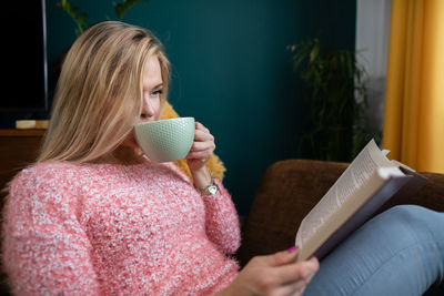 A girl relaxes by reading a book and drinking coffee.