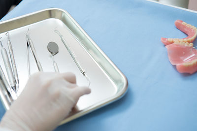 Cropped hand of dentist holding dental equipment in tray on table