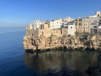 Buildings by sea against clear blue sky