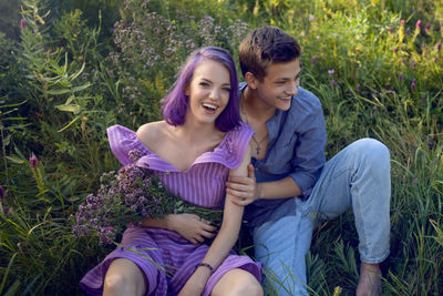 Lovers are a beautiful guy with a girl with purple hair and bouquet of flowers sitting on the grass