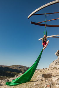 Full length of woman exercising while handing on textile against sky