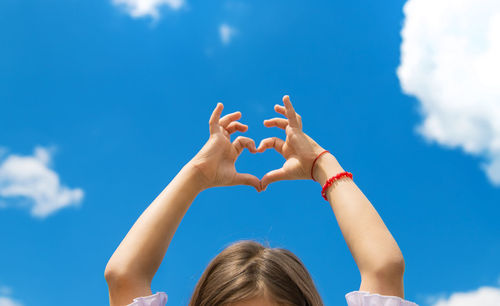 Low angle view of girl making heart shape against sky