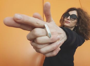 Close-up of woman in sunglasses pointing against orange wall