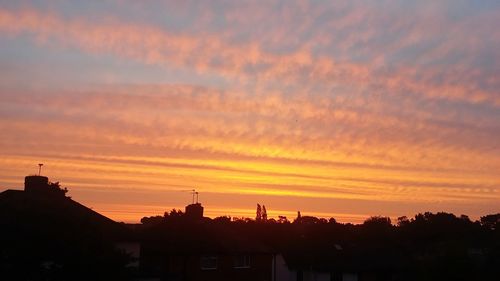 Silhouette houses in town against sky at sunset