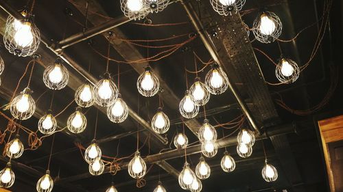 Low angle view of illuminated light bulbs hanging from ceiling