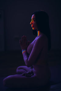 Side view of woman sitting against black background