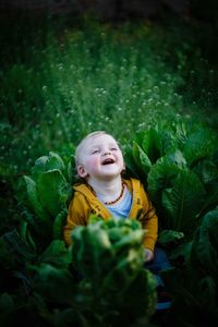 High angle view of baby boy sitting amidst plants on field