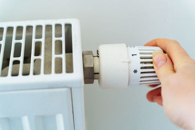Woman's hand switches radiator heating regulator to minimum to save heat energy 