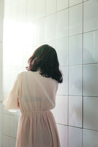 Rear view of woman standing against wall at home