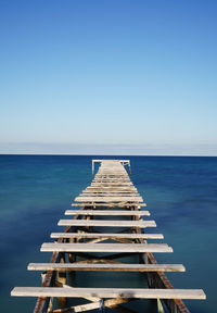 Pier over sea against clear blue sky