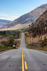 Country road leading towards mountains against sky