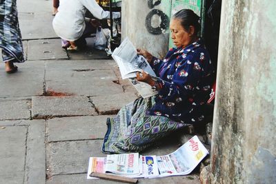 Mature woman reading newspaper while sitting on doorway