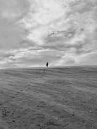 Man walking on beach against cloudy sky