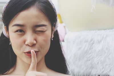 Close-up portrait of young woman with finger on lips winking at home