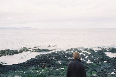 Rear view of man standing on rocky shore