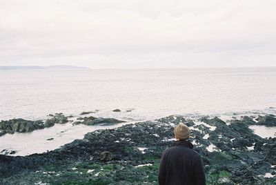 Rear view of man standing in sea against sky