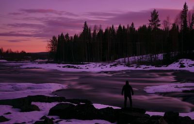 Silhouette person standing on snow covered land against sky during sunset