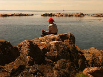 Rear view of woman sitting on rock against sea