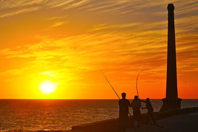 Silhouette of men fishing in sea during sunset