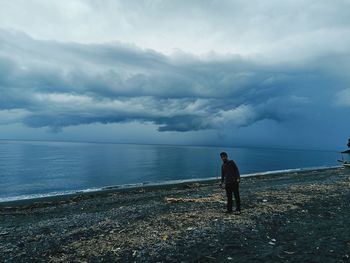 Rear view of  man walking at beach under dramatic sky could, sea landscape and horizons of the earth 