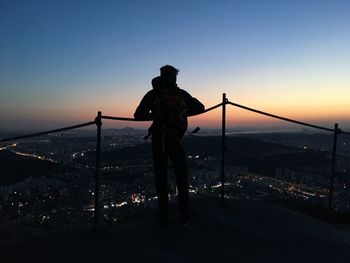 Silhouette man standing by railing against sky at sunset