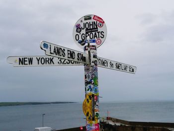 Information sign by sea against sky