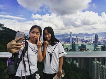 Portrait of smiling young woman using smart phone against sky