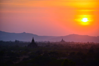 Silhouette temples on field against sky during sunset