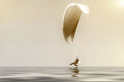 Side view of person paragliding over sea against sky