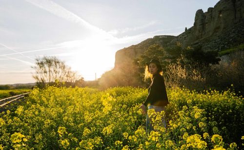 Side view of woman standing by flowering plants on field