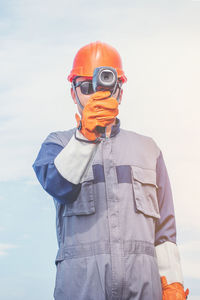 Manual worker holding equipment while standing against sky