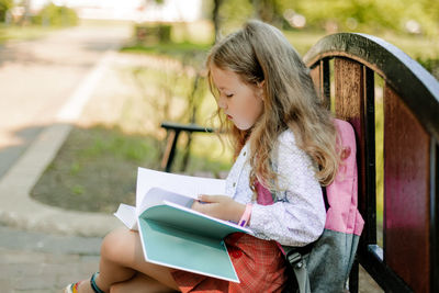 A cute thoughtful schoolgirl is sitting on a bench with books. back to school, lesson schedule