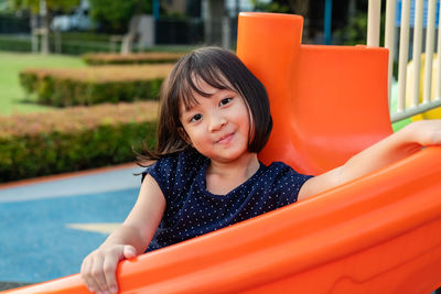Portrait of smiling girl sitting on slide in playground