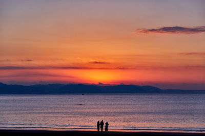 Silhouette people on beach against sky during sunrise