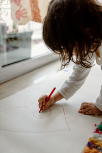 Girl drawing heart shape on paper at home