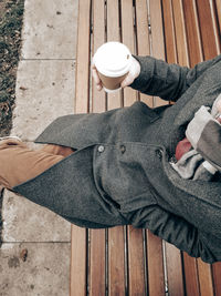 Directly above shot of man drinking coffee while sitting on bench at park