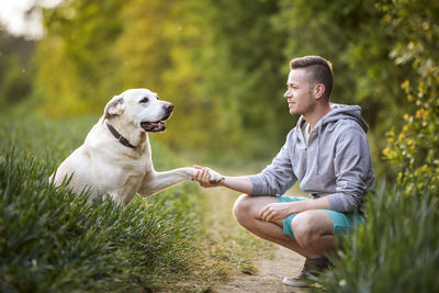 Happy man with dog in nature on sunny summer day. cute yellow labrador retriever giving paw.