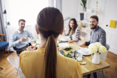 Rear view of woman holding champagne flute while friends sitting at table