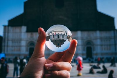Close-up of hand holding crystal ball with city in background - san petronio, bologna