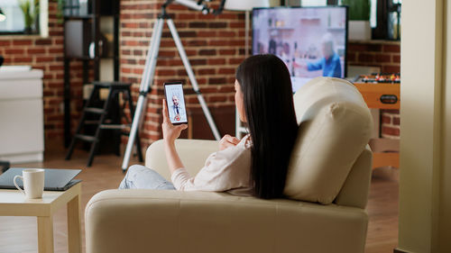 Woman using mobile phone while sitting on sofa at home